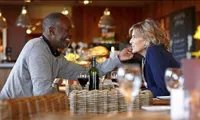 Warm, inviting dining setting with a couple enjoying wine at a table in a rustic restaurant.