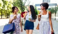three women walking outdoors with shopping bags and smoothies
