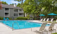 Charming apartment complex with a refreshing outdoor pool, cozy lounge chairs, and vibrant umbrellas amid lush greenery.