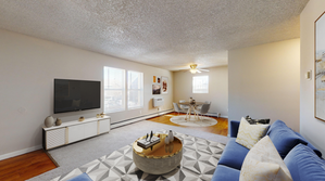 Bright living room with elegant decor, featuring a plush blue sofa, stylish geometric rug, and a dining area with modern table and chairs.