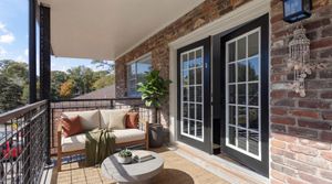 Charming balcony with cozy seating, a lush plant, and elegant glass doors against a rustic brick wall.