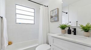 Bright, modern bathroom with elegant white tiles, contemporary artwork, and lush green plants.