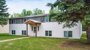 Charming two-story apartment building surrounded by lush greenery, featuring a welcoming entrance and ample natural light.