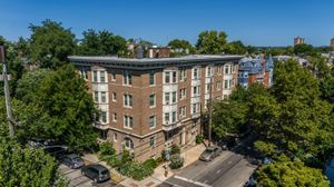 Charming brick apartment building surrounded by lush greenery on a sunny day, showcasing urban living with a touch of nature.