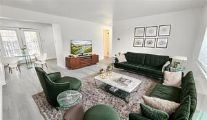 Bright and modern living room with elegant green furniture, cozy shaggy rug, and a wall-mounted TV, connected to a dining area with natural light streaming through large windows.