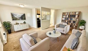 Spacious living room with modern decor, cozy seating area, and stylish bookshelf. Open access to the kitchen adds a touch of elegance.