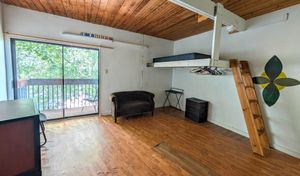 Charming room with a loft bed, cozy seating, and a sliding door leading to a private balcony with lush green views.