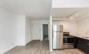 Modern kitchen with stainless steel appliances, sleek dark cabinetry, and stylish lighting on light wood flooring.