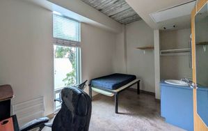 Cozy bedroom featuring a large window, a sleek desk chair, and a minimalist bed with adjacent vanity.