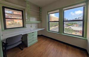 Bright room with large windows offering scenic city views, featuring a built-in desk, shelves, and elegant hardwood floors.