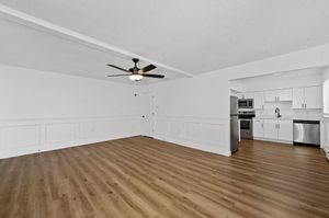 Modern open-concept living area with elegant wooden flooring, ceiling fan, and sleek kitchen featuring stainless steel appliances.