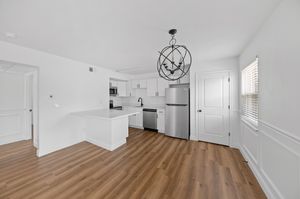 Modern kitchen with sleek white cabinetry, stainless steel appliances, and elegant pendant lighting, set in an open space with beautiful wooden floors.