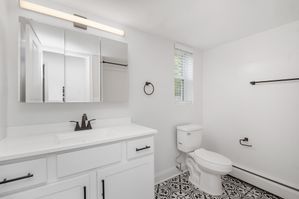 Bright, contemporary bathroom with sleek mirror cabinets, elegant fixtures, and patterned floor tiles.