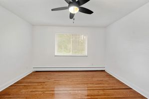 Bright and airy empty room with polished hardwood floors, modern ceiling fan, and large window offering natural light, perfect for a cozy bedroom or home office.