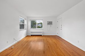 Bright living room with large window, polished hardwood floors, and modern wall unit air conditioner.