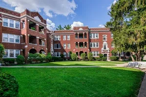 Charming red-brick apartment complex with lush green courtyard and classic architectural details.