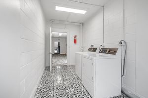 Modern laundry room with stylish black and white patterned floor tiles, featuring a washing machine and dryer set against pristine white walls.