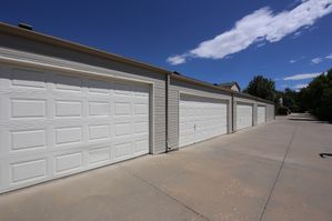 Row of modern garages with pristine white doors under a clear blue sky, offering secure and spacious parking.