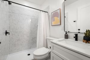 Bright, modern bathroom featuring a marble shower, white vanity with sleek fixtures, and contemporary artwork.