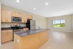 Bright open-concept kitchen with modern stainless steel appliances and large island, seamlessly flowing into a sunlit living area with scenic window views.