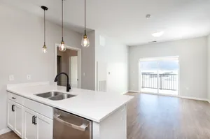 Bright modern kitchen with sleek white countertops, stylish pendant lighting, and open-concept living area leading to a balcony with scenic views.