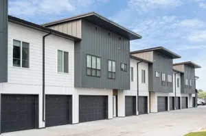 Modern multi-story townhouses with sleek design and spacious garages under a bright blue sky.