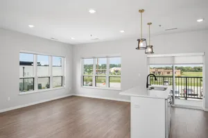 Bright, open-concept apartment with floor-to-ceiling windows, modern lighting, and a stylish kitchen island with sink, overlooking peaceful views.