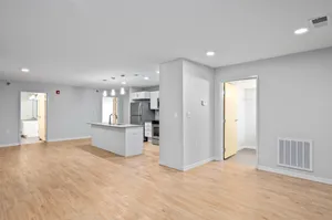 Modern open-concept apartment interior with sleek kitchen island, light wood flooring, and spacious rooms.