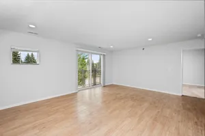 Bright living room with elegant hardwood floors, large sliding glass doors leading to a balcony, and a neutral color palette for a spacious feel.