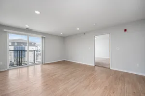 Bright and spacious living room with modern wooden flooring, large windows offering plenty of natural light and a view of the surrounding area, leading to a cozy adjacent room.