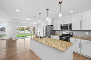 Bright, modern kitchen with granite countertops and stainless steel appliances, overlooking a spacious living area with large windows and natural light.
