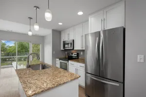 Modern kitchen with granite countertops, stainless steel appliances, and pendant lighting, overlooking a scenic balcony view.