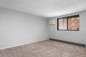 Bright and spacious room with neutral walls, soft carpet, and large window offering natural light.