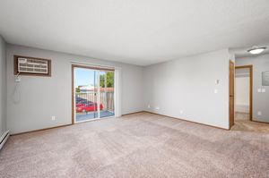 Bright and spacious living room with plush carpeting, large window, and sliding glass door opening to a private balcony.