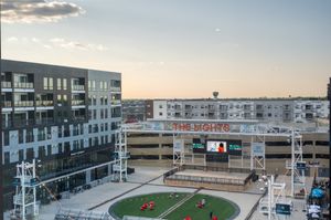 Vibrant urban complex with a modern residential building overlooking an inviting plaza and entertainment stage at sunset.