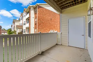 Charming apartment balcony with a white railing, offering picturesque views of a sunny residential neighborhood with brick buildings.