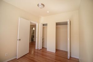 Bright empty bedroom featuring hardwood floors, double closets, and a peek into the adjacent bathroom.