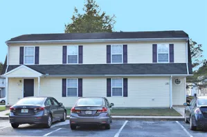 Charming two-story residential building with a neatly manicured lawn and convenient parking spaces in front, featuring classic architectural details.