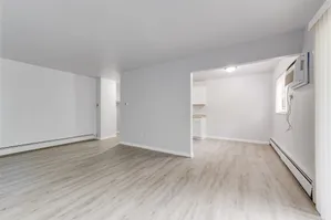 Inviting open-concept living area with light wood flooring and modern finishes, leading into a cozy kitchen space.