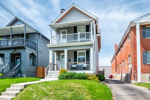 Charming two-story house with elegant front porch and manicured lawn, nestled between neighboring homes under a clear blue sky.