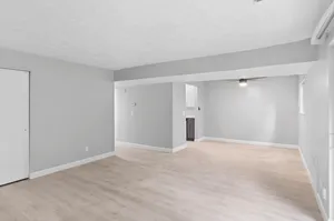 Spacious open floor plan with light wood flooring, modern gray walls, and a cozy ceiling fan in a bright living area.