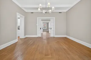 Elegant living space featuring hardwood floors, classic chandelier, and double doors opening to a sunlit room.