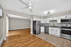 Inviting open-concept kitchen and living area with sleek stainless steel appliances, elegant white cabinetry, and warm hardwood flooring.