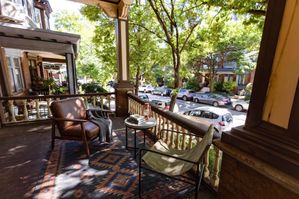 Charming outdoor porch with comfortable seating, surrounded by lush greenery, offering a serene view of the tree-lined street below.