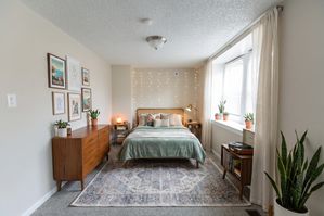 Charming bedroom with a cozy bed, soft lighting, and elegant decor. Features a stylish dresser, indoor plants, and large windows for natural light.