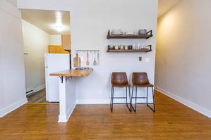 Modern kitchen nook featuring wooden bar counter, stylish shelving, chic bar stools, and cozy atmosphere.