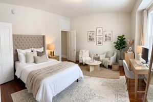 Elegant bedroom showcasing a plush bed with tufted headboard, cozy seating area, and chic workspace, accented by soft lighting and natural decor.