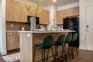 Modern kitchen with elegant wooden cabinetry, sleek black appliances, and an island featuring dark green stools and decorative accents.
