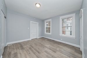 Bright and airy room with elegant laminate flooring, soft gray walls, and abundant natural light from double windows.