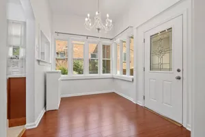 Bright and inviting corner space with elegant chandelier, large windows, and polished wood flooring, perfect for dining or relaxation.